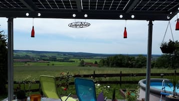 Un espacio de estar al aire libre cubierto con vistas a una piscina y al campo.