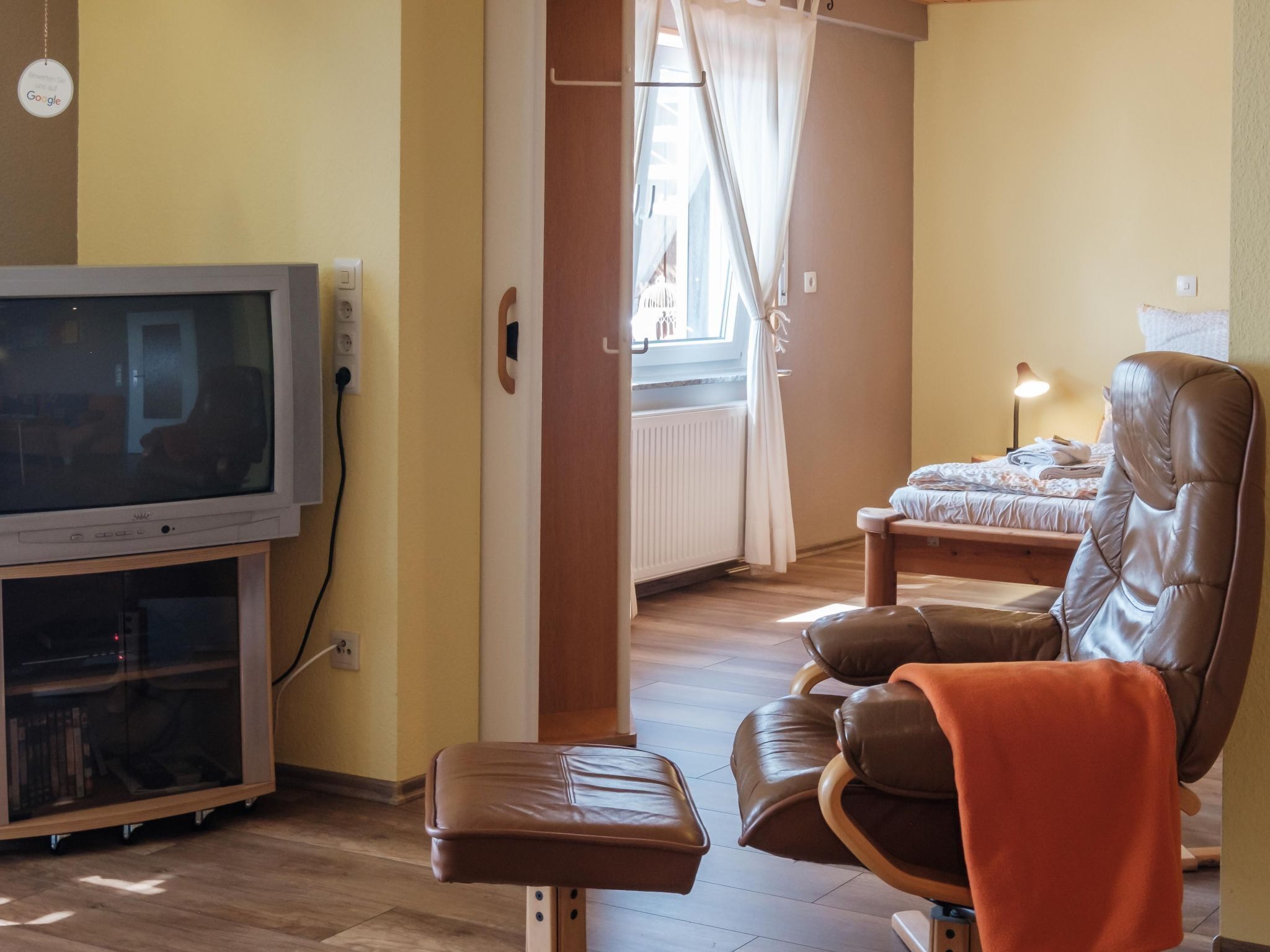Een kamer met een televisie, een leren fauteuil, een bed en een raam met gordijnen.