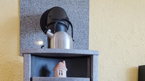 Ein Kaminofen mit Glastür, eine kleine hauseförmige Dekoration darauf und ein Holzkorb daneben.