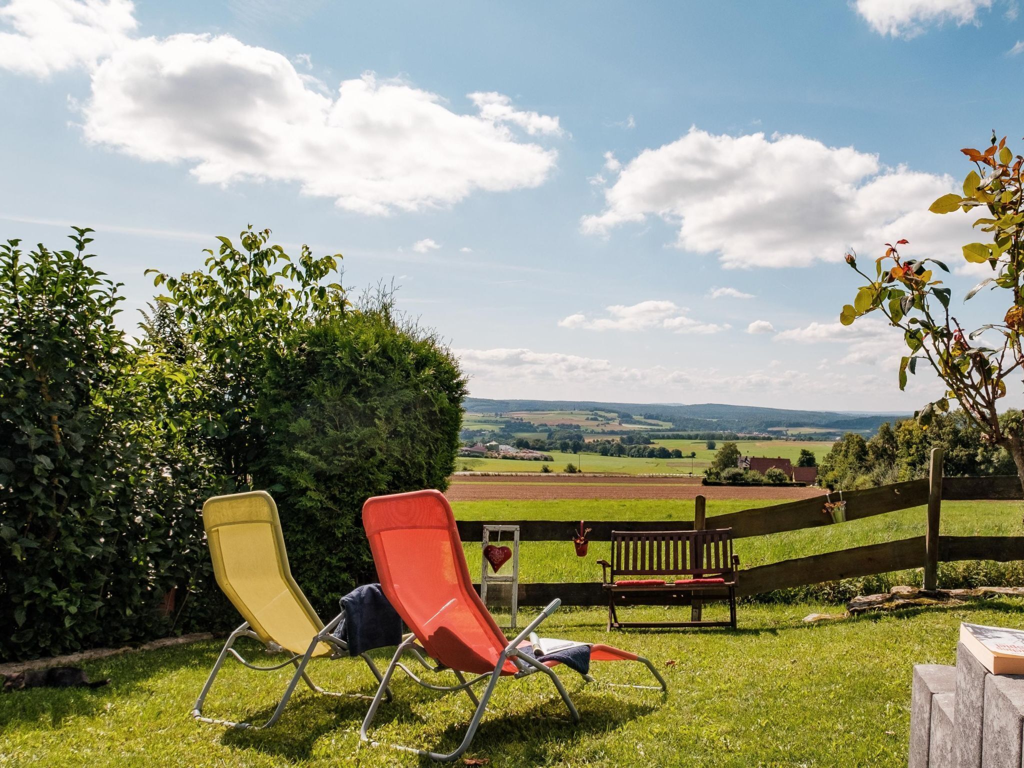 Un espacio al aire libre con césped, dos sillones de relax y un banco de madera.