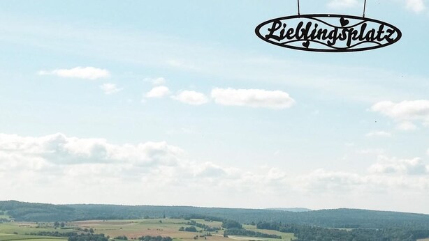Ein Terrassenstuhl mit Blick auf eine ländliche Landschaft, darunter Felder und Hügel.