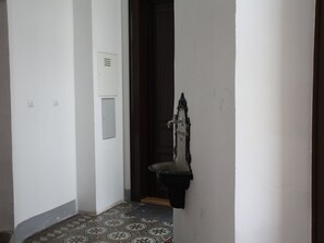 A narrow hallway with a tiled floor, a white wall with a light switch, and a door with a metal handle. - Wohnen am Augarten by Interhome (Vienna)