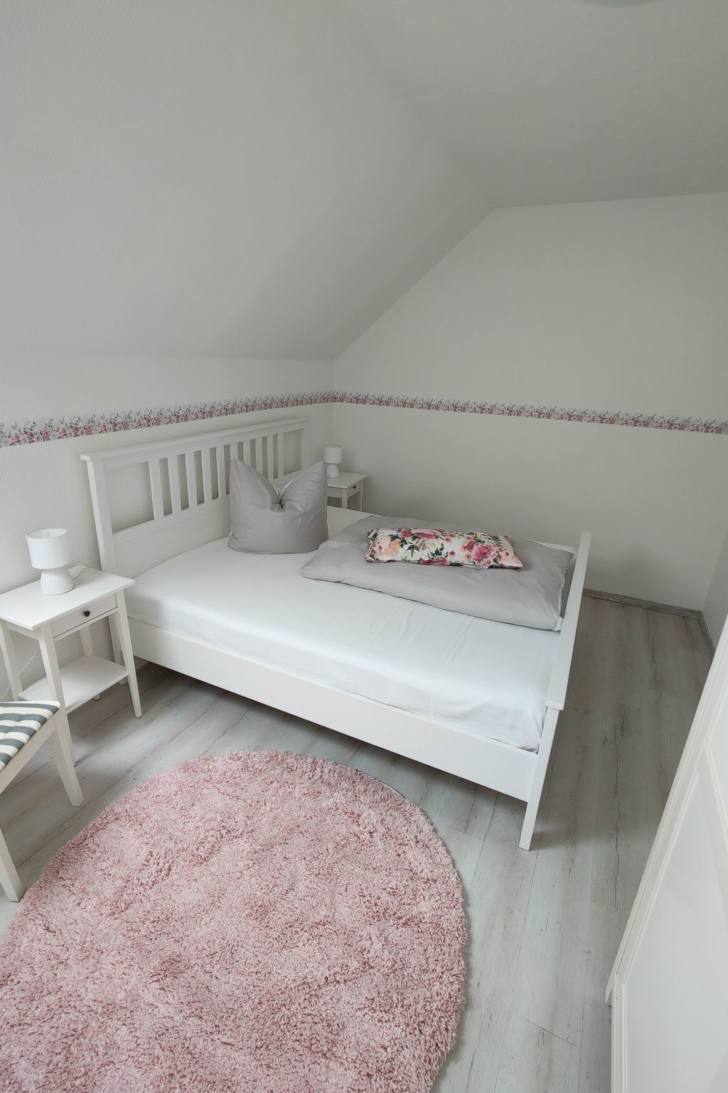 A bedroom with a white bed, a small bedside table, a lamp, and a pink rug.