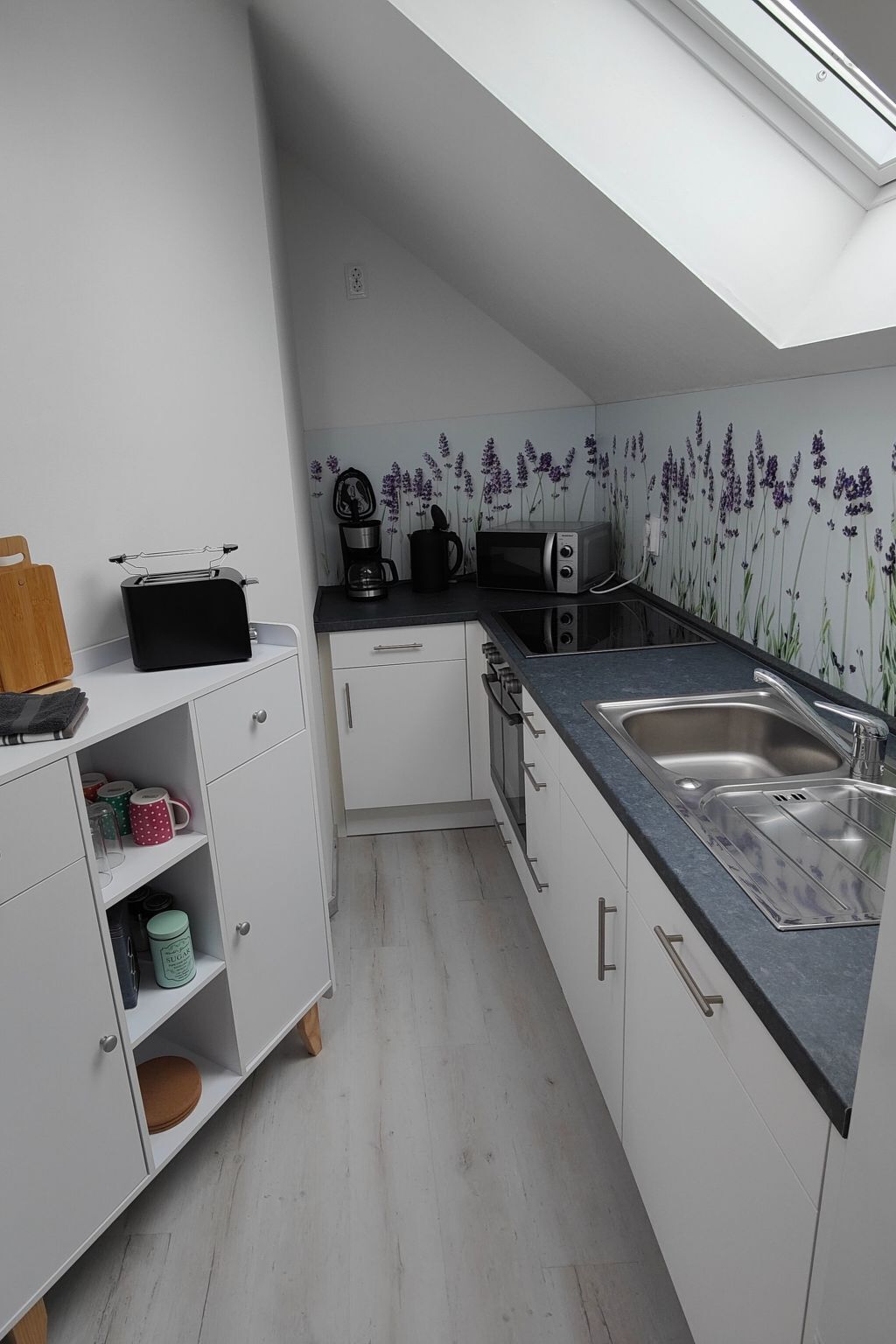 A compact kitchen with white cabinets, a black countertop, a microwave, a coffee maker, and a toaster.