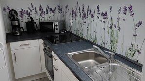 A modern kitchen with white cabinets, a black countertop, a stainless steel sink, a microwave, and a coffee maker. - Urlaubszuhause by Interhome (Naundorf)