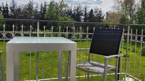 A table and chair set on a balcony with a metal railing, overlooking a grassy area with trees and a clear sky. - Urlaubszuhause by Interhome (Naundorf)