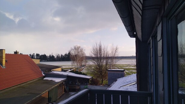 A view from a balcony overlooking a snowy landscape with a river and distant trees. - Ferien- und Monteurwohnung Nepperwitz Süd by Interhome (Bennewitz)