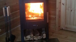 A wood-burning stove with a visible fire, set against a wooden wall. - Järvstuga by Interhome (Arvidsjaur)