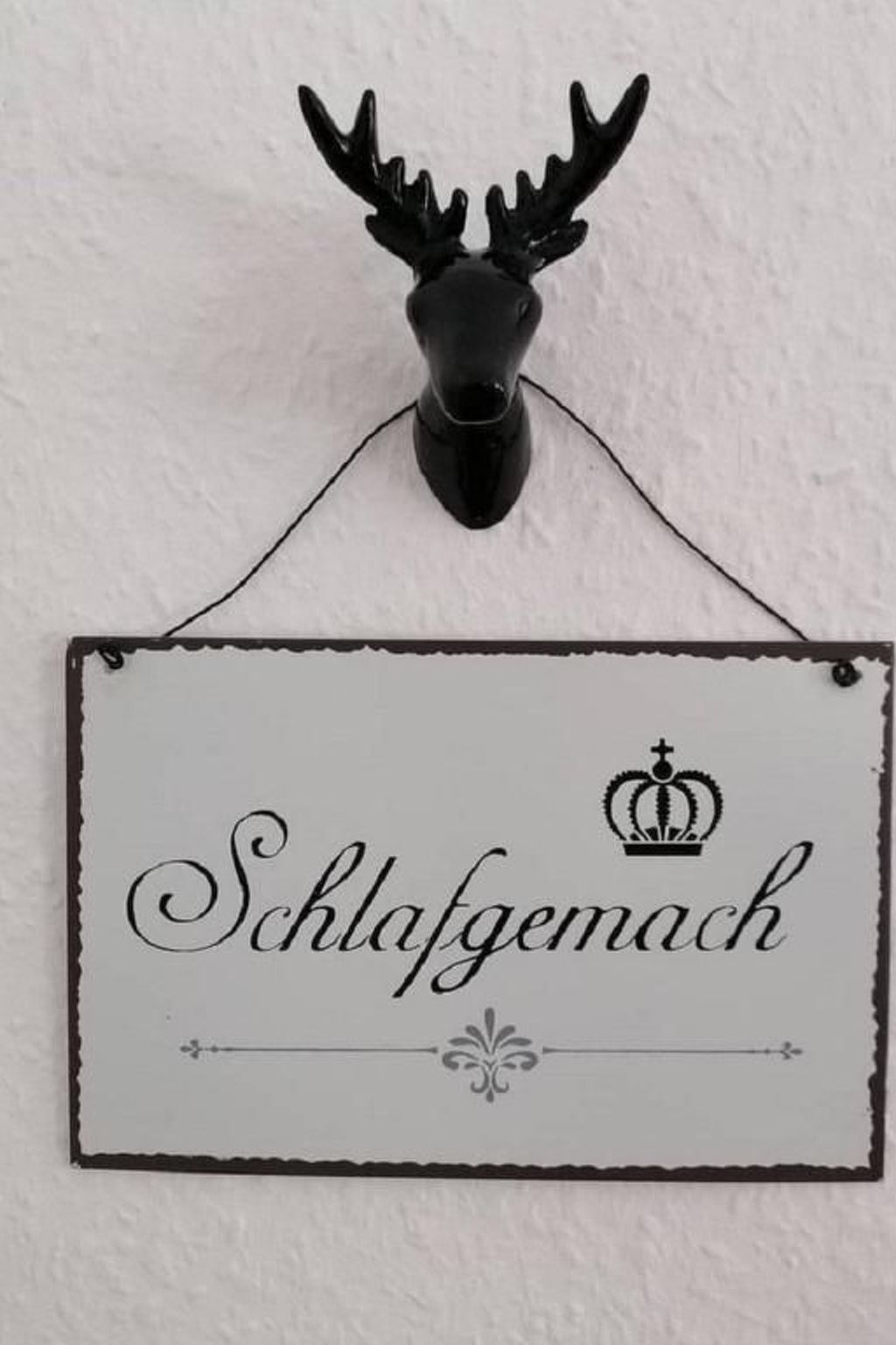 Une enseigne portant le mot « Schlafgemach » et un symbole de couronne, fixée au mur au-dessus d’une tête de cerf noire.