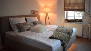 Un dormitorio con una cama, una lámpara de noche, una ventana con persianas y un radiador.