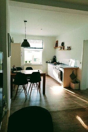 A modern kitchen with a dining area, wooden flooring, and a hanging pendant light. - Stadt Apartement by Interhome (Geisa)