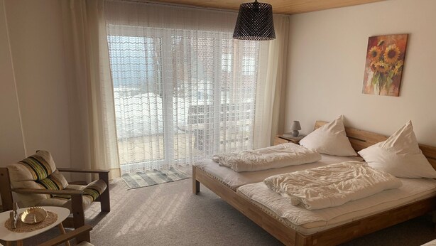 Une chambre à coucher avec un lit, deux chaises, une petite table, une lampe et un tableau au mur.