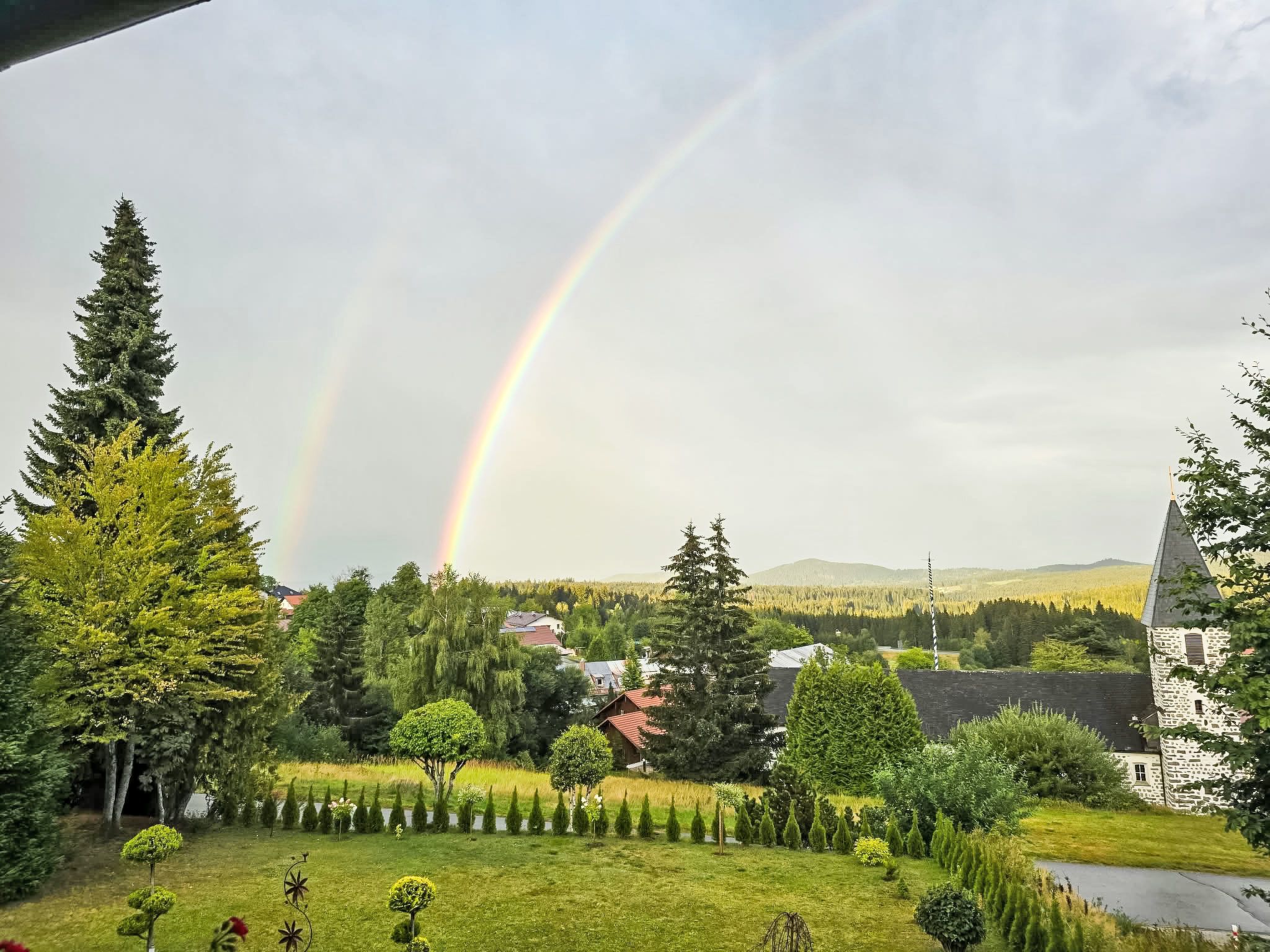 A rural landscape with a rainbow, houses, and a church.