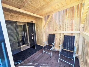 Une terrasse en bois avec deux chaises et un espace sauna fermé par des parois de verre.
