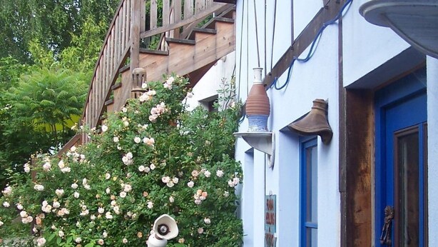 En traditionell byggnad med en blå dörr, en trätrappa och en trädgård med rosa blommor.