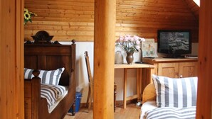 En mysig stuga med träväggar och trägolv, en sovplats i loftstil med två sängar, ett skrivbord med en tv och ett stort fönster som släpper in naturligt ljus.