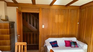 Ein gemütlicher Raum mit einer Holztreppe, einem weißen Sofa mit bunten Kissen, einem Holztisch und einem Schrank.