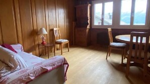 Ein Zimmer mit einem Bett, einem Tisch, Stühlen, Holzwänden und einem Fenster mit Aussicht.
