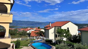 A residential area with a swimming pool, houses with red roofs, and a view of distant mountains under a clear blue sky. - Apartment PintaDeSol by Interhome (Krk/Čižići)