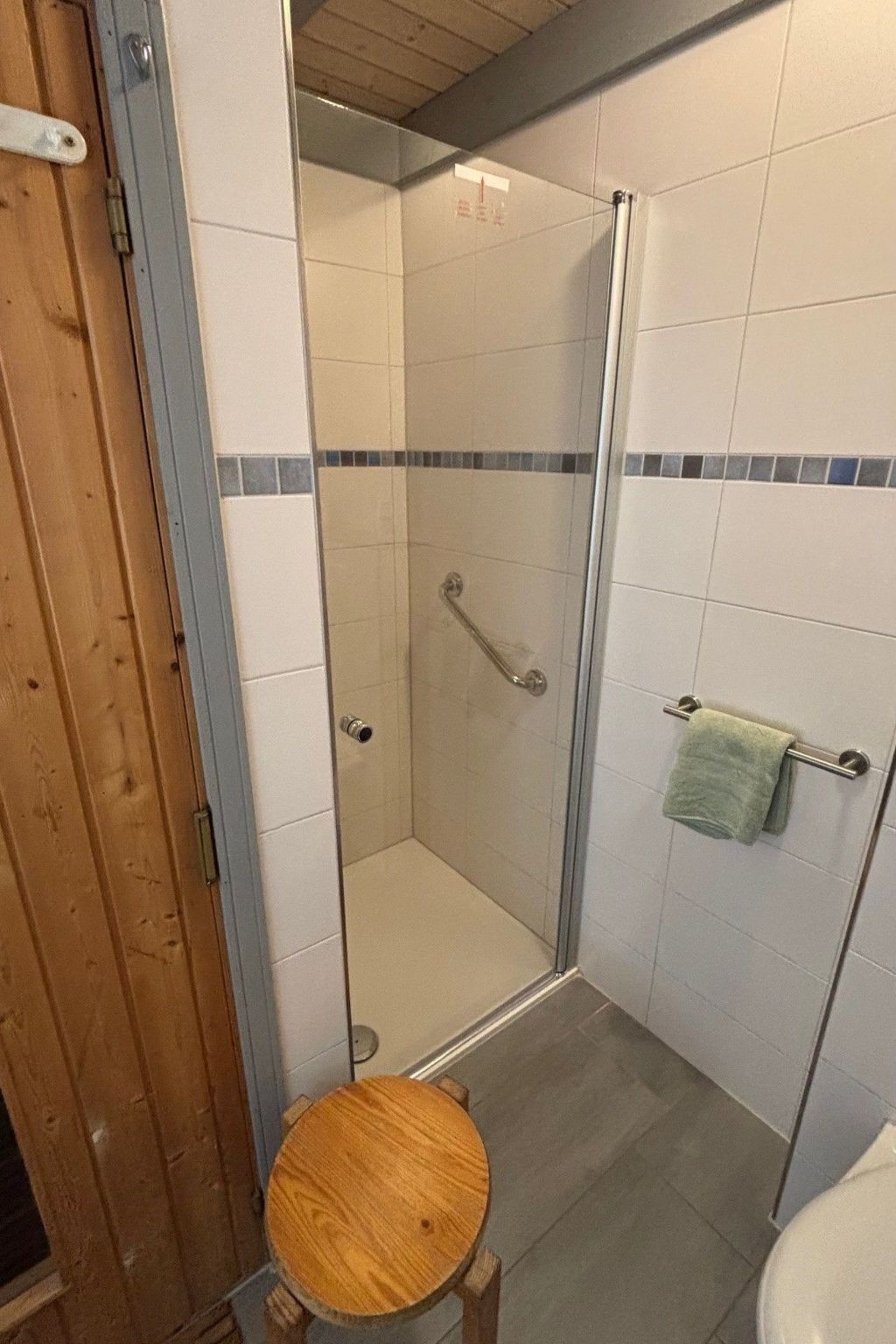 Une douche avec une porte en verre, un tabouret en bois et un porte-serviettes avec une serviette.