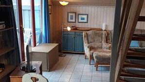 En hyggelig stue med et træbord, stole og en sofa. Der er en trappe, der fører op til en etage.
