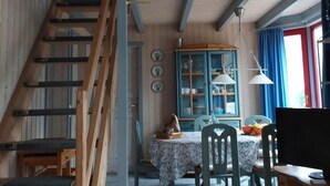 Et hyggeligt rum med en trætrappe, et spiseområde med bord og stole, og et vindue med gardiner.