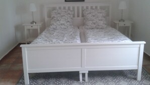 Una cama blanca con ropa de cama floral, dos mesitas de noche con lámparas y un cuadro en la pared.