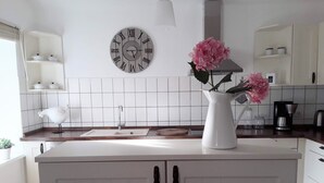 Una cocina moderna con armarios blancos, encimera blanca, un reloj decorativo y un florero con flores.