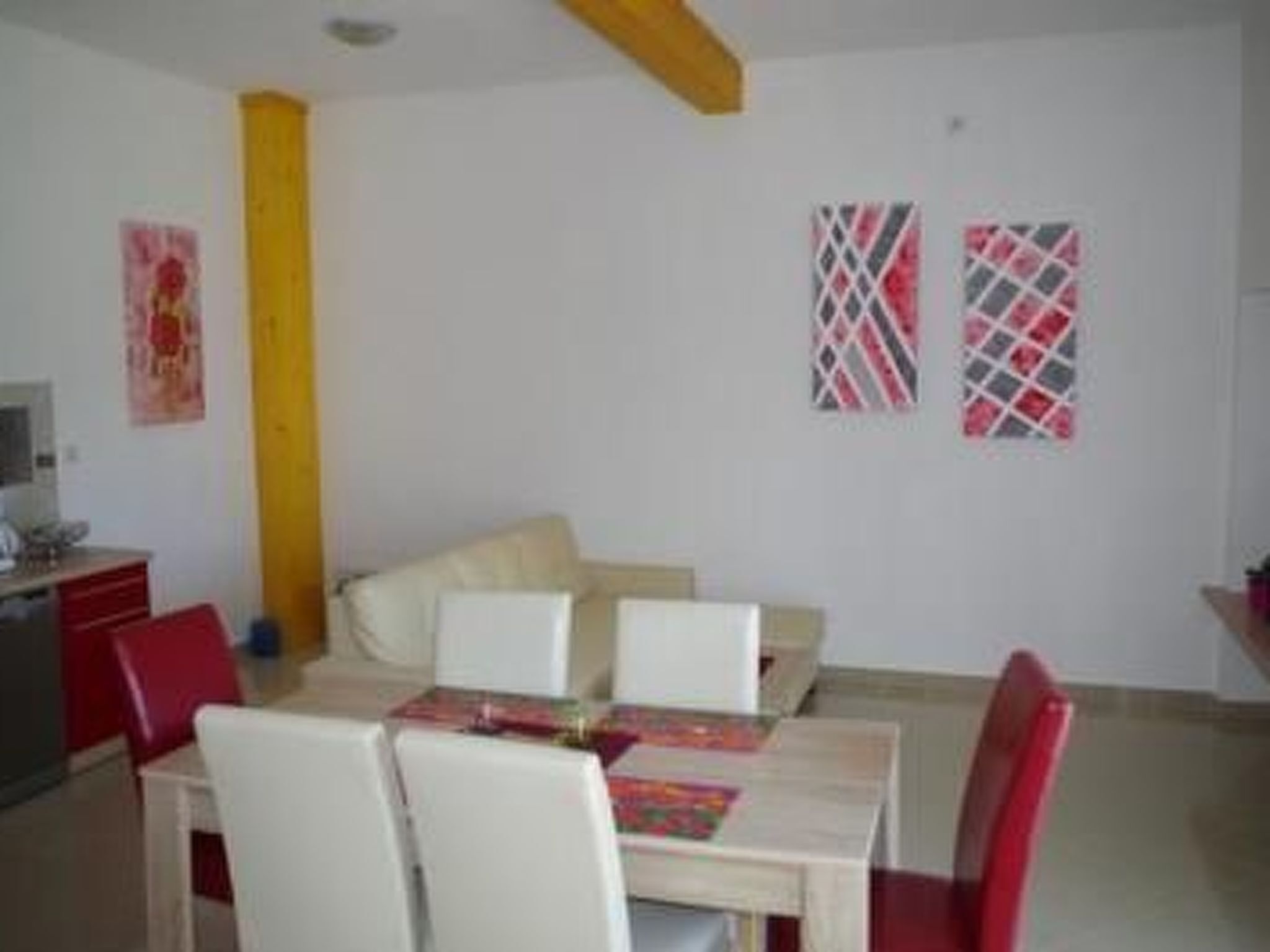 A dining area with a table and chairs, a yellow column, and two patterned wall hangings.