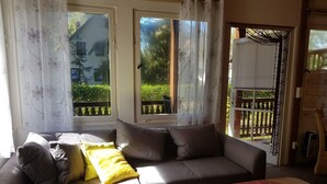 A living room with a sofa, yellow and gray cushions, a small table with a red cloth, and large windows with curtains. - mit Wallbox by Interhome (Diensdorf-Radlow)