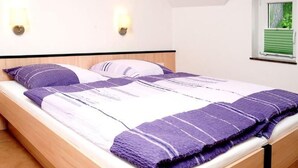 A single bed with a wooden frame, white bedding, and purple accents. There are two wall-mounted lights and a window with blinds. - Beim Kahnfährmann by Interhome (Schlepzig)