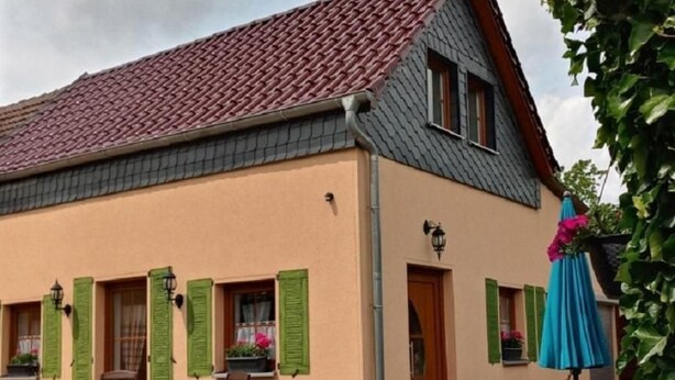 A building with a sloped roof, green shutters, and outdoor seating with tables and chairs. - - Uns lütt Hüsung by Interhome (Löwenberger Land)