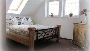 A bedroom with a sloped ceiling, a bed with floral bedding, two windows with curtains, and a wooden cabinet. - - Uns lütt Hüsung by Interhome (Löwenberger Land)