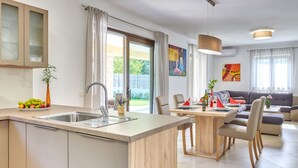 Una cucina moderna con isola centrale, una zona pranzo con tavolo in legno e un soggiorno con divano e poltrone.