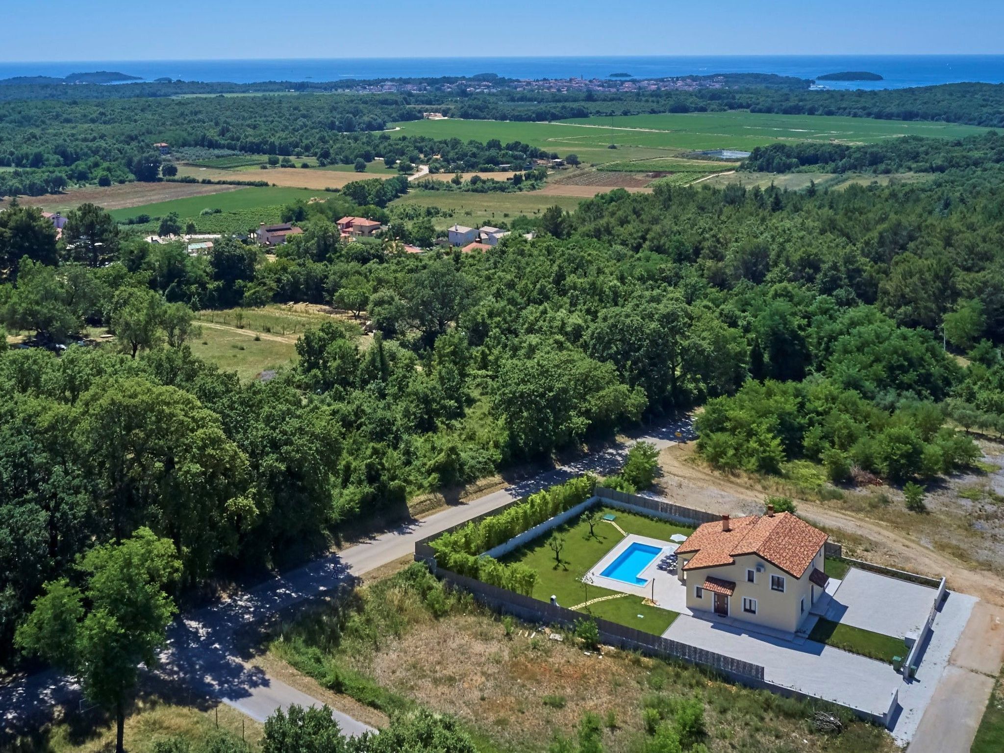 An aerial view of a property with a swimming pool, surrounded by dense greenery and a coastal backdrop.