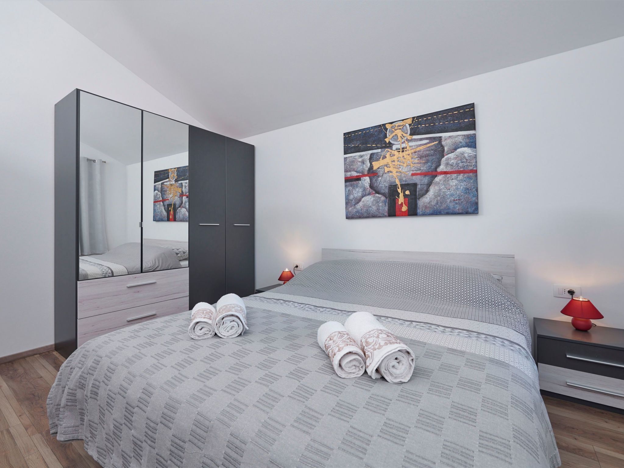 Une chambre moderne avec un grand lit, une armoire, un miroir et un tableau accroché au mur.