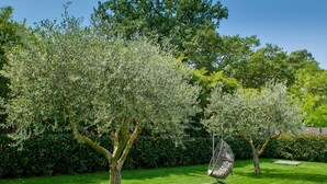 Un giardino curato con alberi maturi, una sedia a dondolo e un prato ben tagliato.