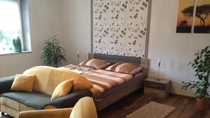 A bedroom with a bed, a sofa, a nightstand, a lamp, and a window with plants. - in Neustrelitz mit Garten und Grill by Interhome (Neustrelitz)