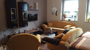 A modern living room with a sofa set, a flat-screen TV, decorative items, and a window with a view. - in Neustrelitz mit Garten und Grill by Interhome (Neustrelitz)