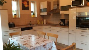 A kitchen with white cabinets, a microwave, an oven, a coffee maker, and a table with a floral tablecloth. - in Neustrelitz mit Garten und Grill by Interhome (Neustrelitz)