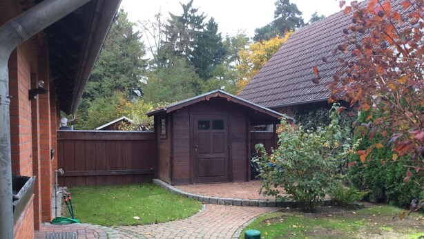 A brick house with a wooden garage, a paved driveway, and a green fence. - in Neustrelitz mit Garten und Grill by Interhome (Neustrelitz)