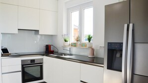 A modern kitchen with white cabinetry, a stainless steel refrigerator, a built-in oven, and a window with potted plants. - mit Blick auf das Wasser by Interhome (Poreč/Nova Vas)