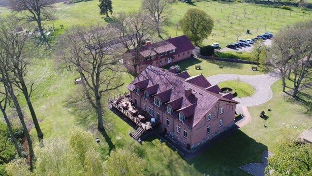 A large, rectangular building with a red-tiled roof, surrounded by green fields and trees. - in Göhren mit Eigener Terrasse by Interhome (Barnin)