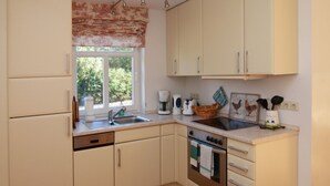 A compact kitchen with white cabinets, a built-in oven, a sink, and a window with a floral valance. - in Göhren mit Eigener Terrasse by Interhome (Barnin)