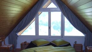 A room with a sloped ceiling, a bed with green bedding, two nightstands, and a window with curtains. - Churfirsten by Interhome (Unterwasser)