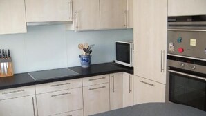 A modern kitchen with light-colored cabinets, a black countertop, a microwave, and an oven. - Churfirsten by Interhome (Unterwasser)