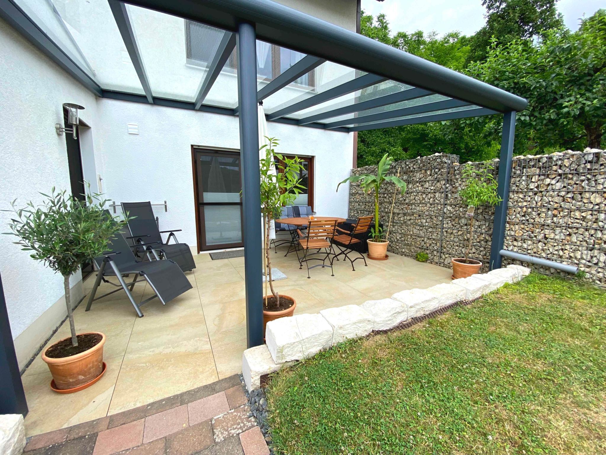 A covered patio with a table and chairs, potted plants, and a stone wall.