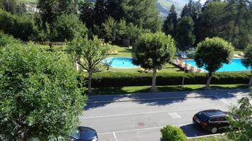 A parking lot with two cars, a swimming pool, and a view of a mountainous landscape.