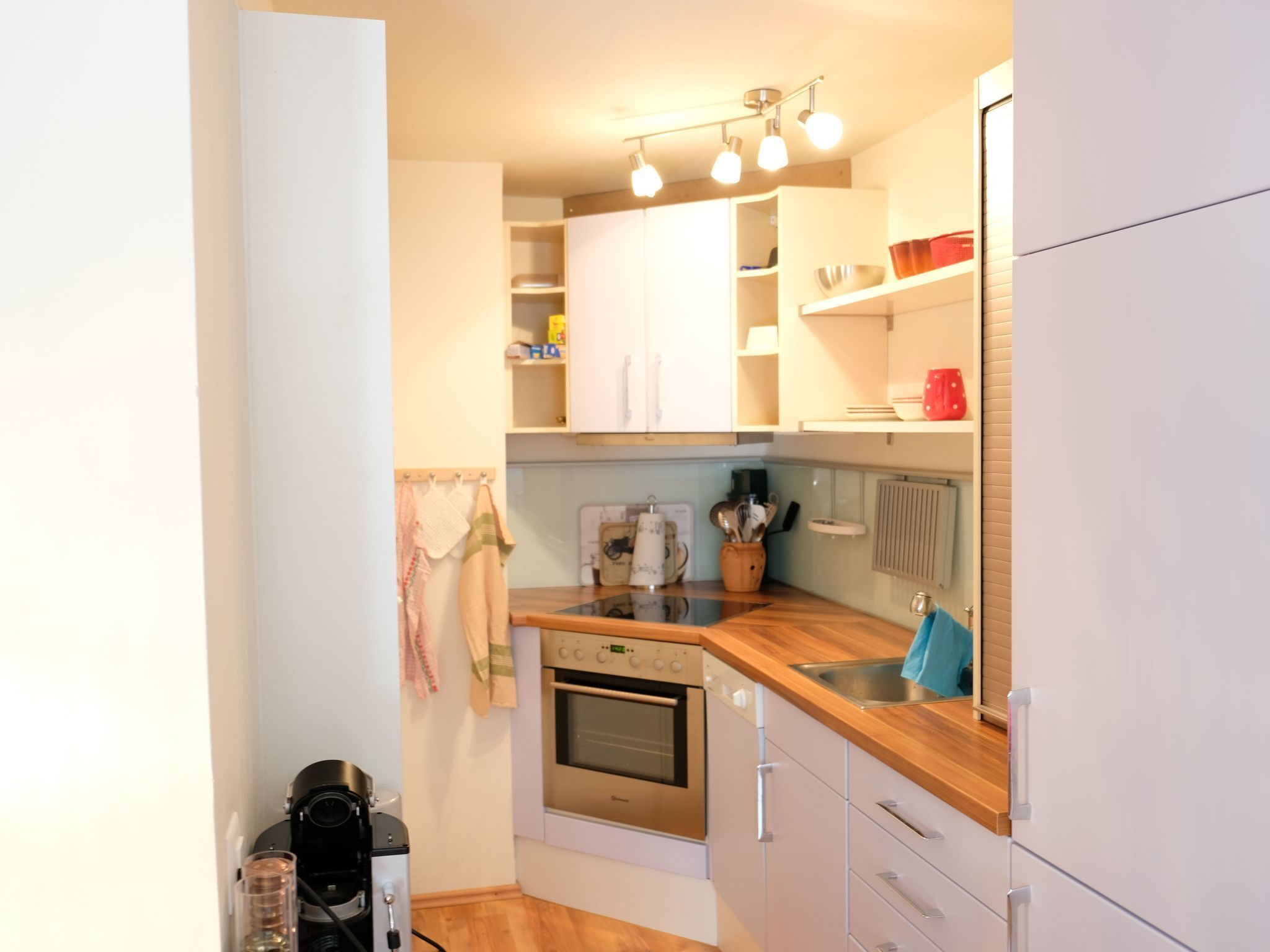 Una cocina compacta con armarios blancos, encimera de madera y horno empotrado.