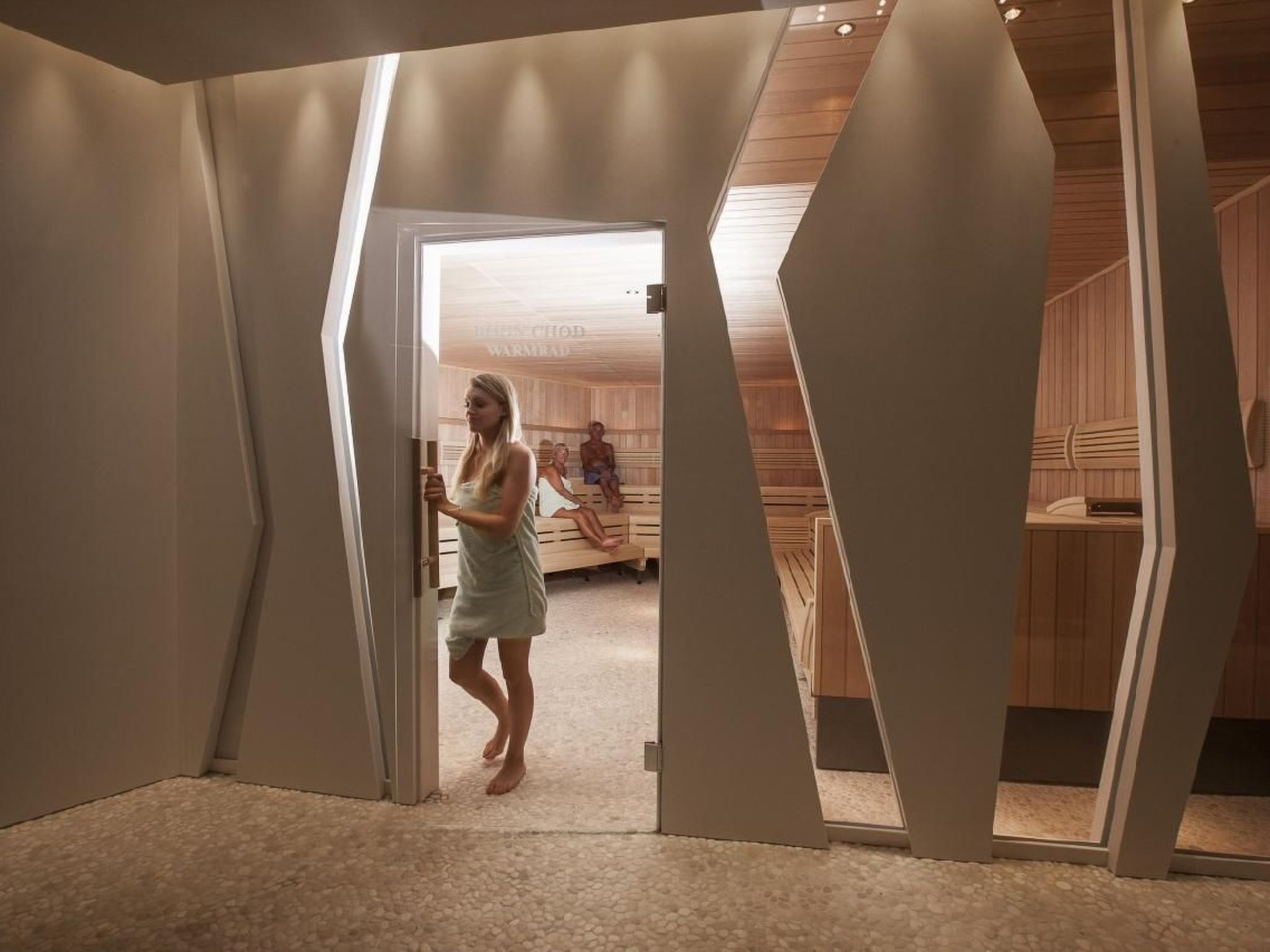 Un interior moderno con un diseño geométrico único, un área de sauna visible y una persona entrando en la habitación.